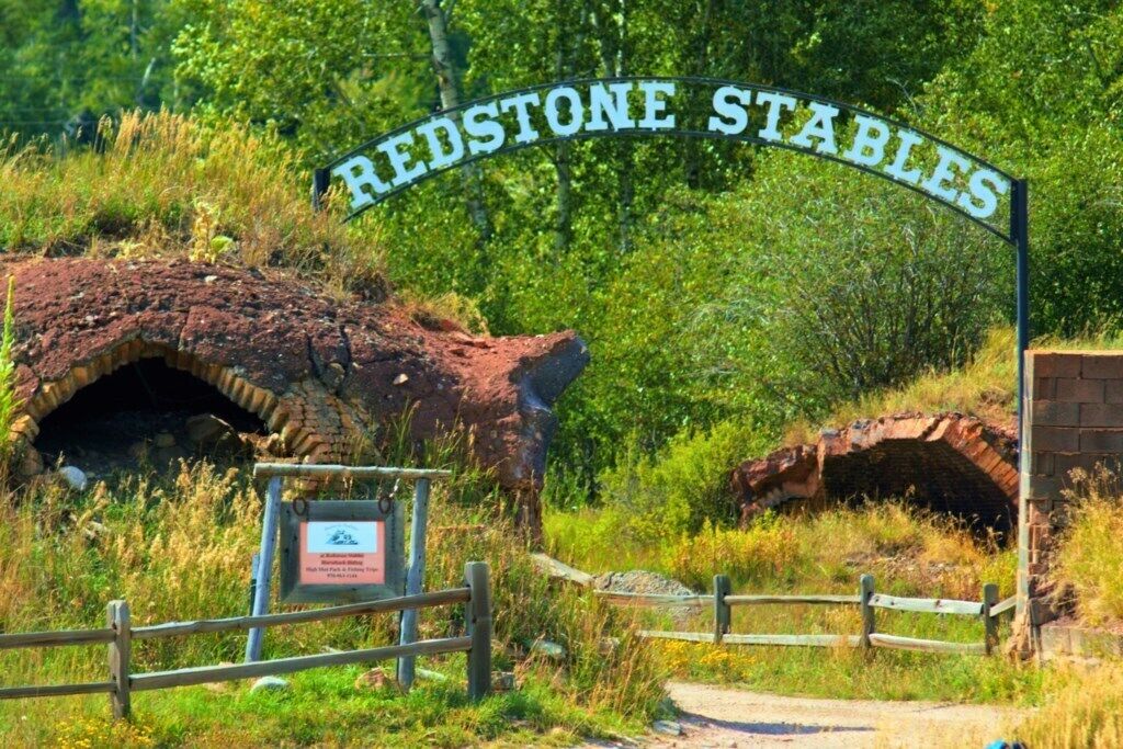 A sign reading "Redstone Stables" with a wooden fence and a brick structure in the background.