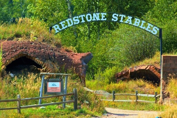 Un letrero que dice 'Redstone Stables', con una valla de madera y una estructura de ladrillo al fondo.