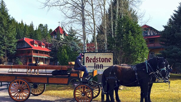 A horse-drawn carriage parked in front of a historic landmark, Redstone Inn, with a sign indicating its name and a view of surrounding buildings.