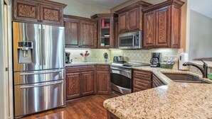 Cocina con armarios de madera, electrodomésticos de acero inoxidable y encimeras de granito.
