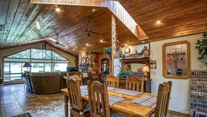 A rustic dining area with wooden furniture, a stone fireplace, and a large window overlooking a deck. - 18802 - 2 Granada Way (Hot Springs Village)