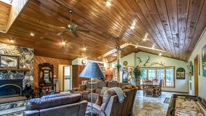 A spacious living room with a wooden ceiling, a fireplace, a sofa, and a dining area. - 18802 - 2 Granada Way (Hot Springs Village)