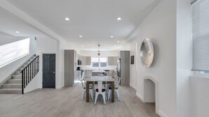 A spacious kitchen with a central island, a dining area with a table and chairs, a staircase, and a large window. - Paradise Cove  (Long Beach)