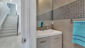 A modern bathroom with a white sink, a mirror, and a tiled shower wall. - Paradise Cove  (Long Beach)