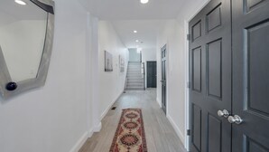 A hallway with a patterned rug, a dark door, and a staircase in the background. - Paradise Cove  (Long Beach)