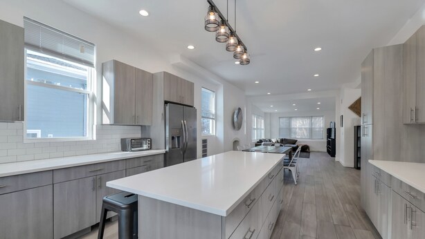 A modern kitchen with a large island, stainless steel appliances, and a contemporary light fixture. - Paradise Cove  (Long Beach)