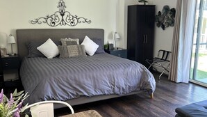 A modern bedroom with a large bed, a wooden table, a dark wardrobe, and a view of the outdoors. - Riverside Mountain Retreat, Ruby of the Rockies (Redstone)