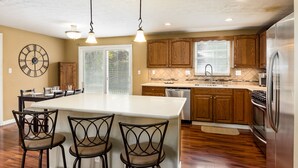 A kitchen with wooden cabinets, a large island with bar stools, a clock on the wall, and a stainless steel refrigerator. - COMPLETELY UPDATED 4 bedroom, 2 full bath home with deck and big yard (Columbus)