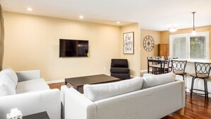 A living room with a sofa, a coffee table, a TV, and a dining area with chairs and a table. - COMPLETELY UPDATED 4 bedroom, 2 full bath home with deck and big yard (Columbus)