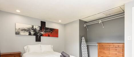 A bedroom with a bed, a wooden dresser, a closet with a hanging rod, and a wall-mounted artwork.