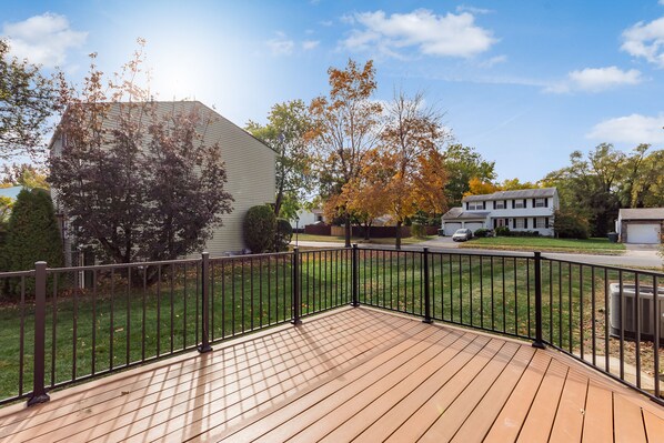 A wooden deck with a black metal railing, a grassy yard, and houses in the background. - COMPLETELY UPDATED 4 bedroom, 2 full bath home with deck and big yard (Columbus)