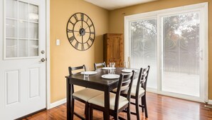 A dining room with a wooden table set for four, a large wall clock, and a sliding glass door leading to a patio. - COMPLETELY UPDATED 4 bedroom, 2 full bath home with deck and big yard (Columbus)