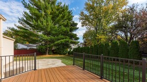 A wooden deck with a metal railing, surrounded by a well-maintained lawn and trees. - COMPLETELY UPDATED 4 bedroom, 2 full bath home with deck and big yard (Columbus)