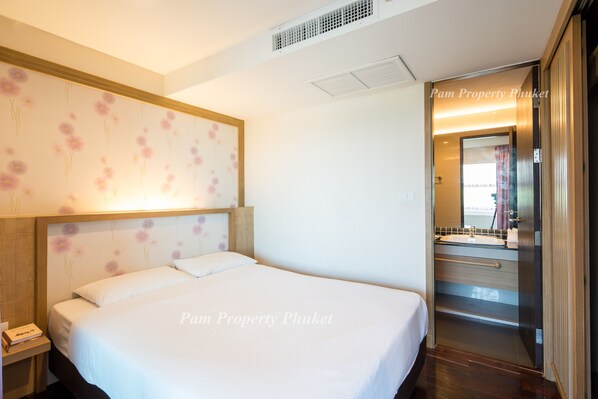 A hotel room with a bed, a nightstand, a wall with floral wallpaper, and a bathroom visible through an open door.
