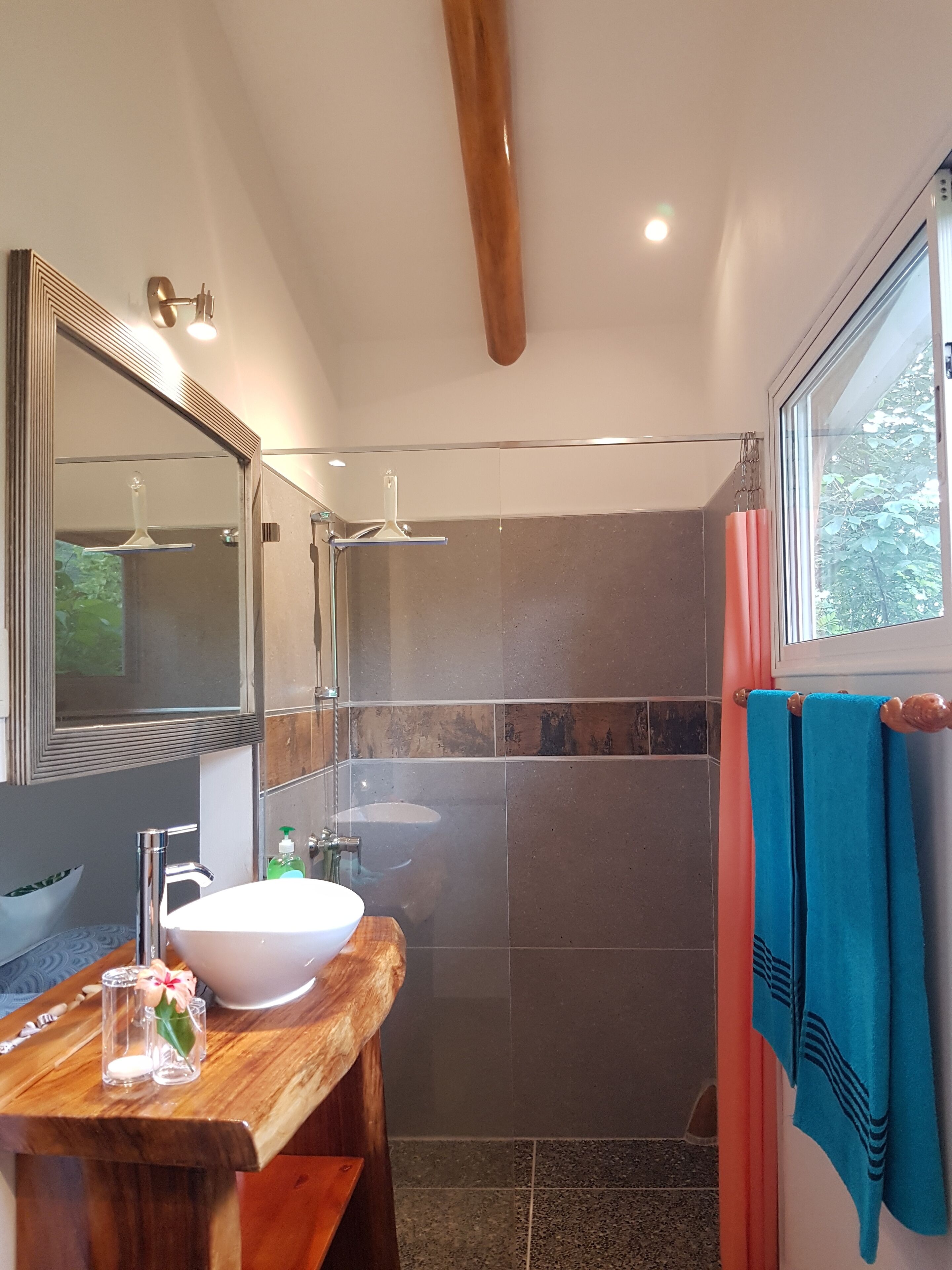 A modern bathroom with a wooden vanity, a large mirror, a white sink, and a shower area.