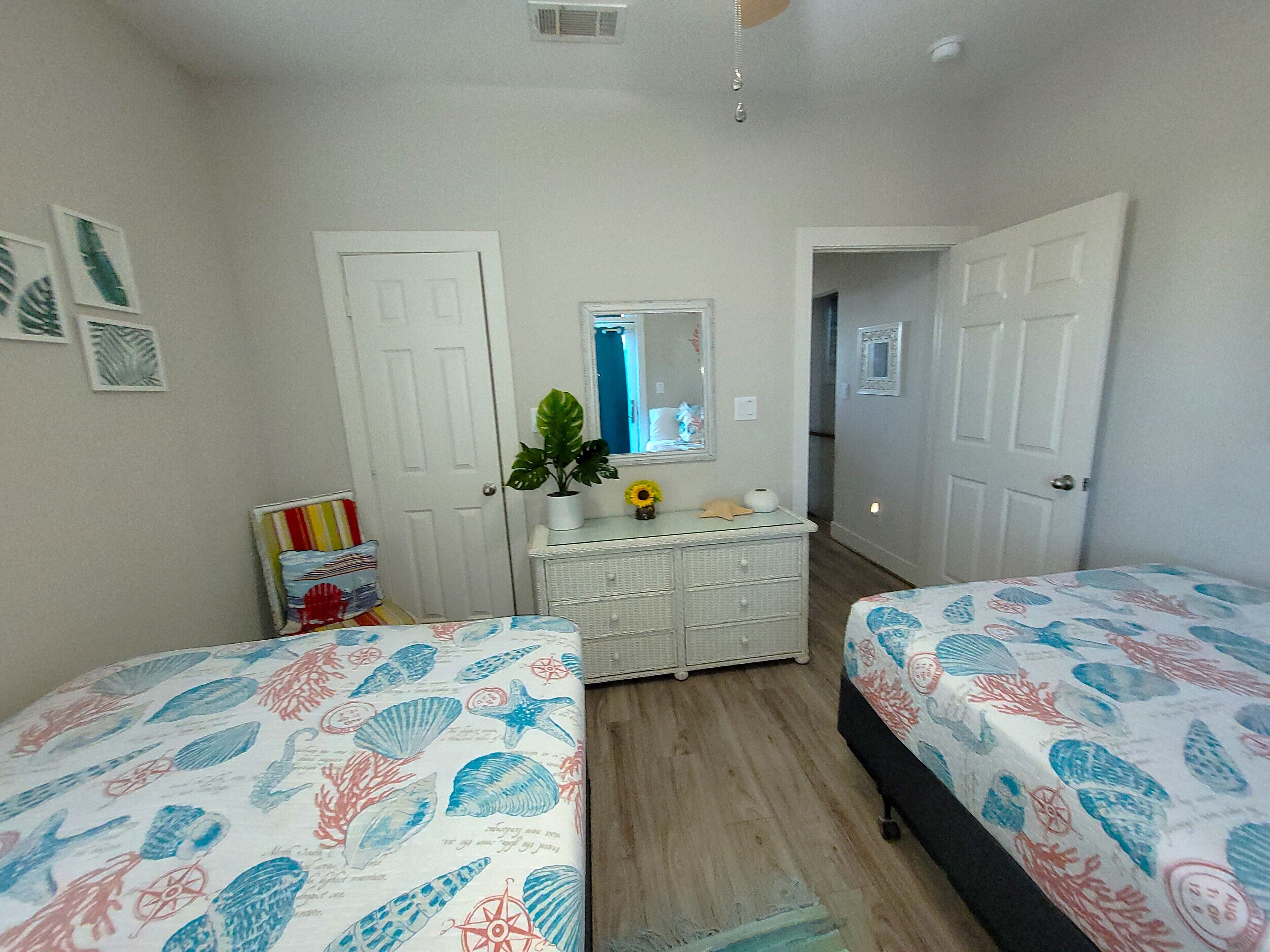 A bedroom with two beds, a dresser, a mirror, and a door leading to another room.
