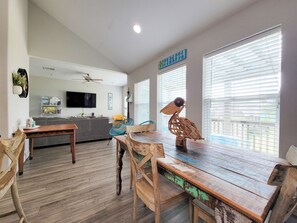 Un salón espacioso con una mesa de comedor de madera, sillas, un sofá y un televisor fijado a la pared.