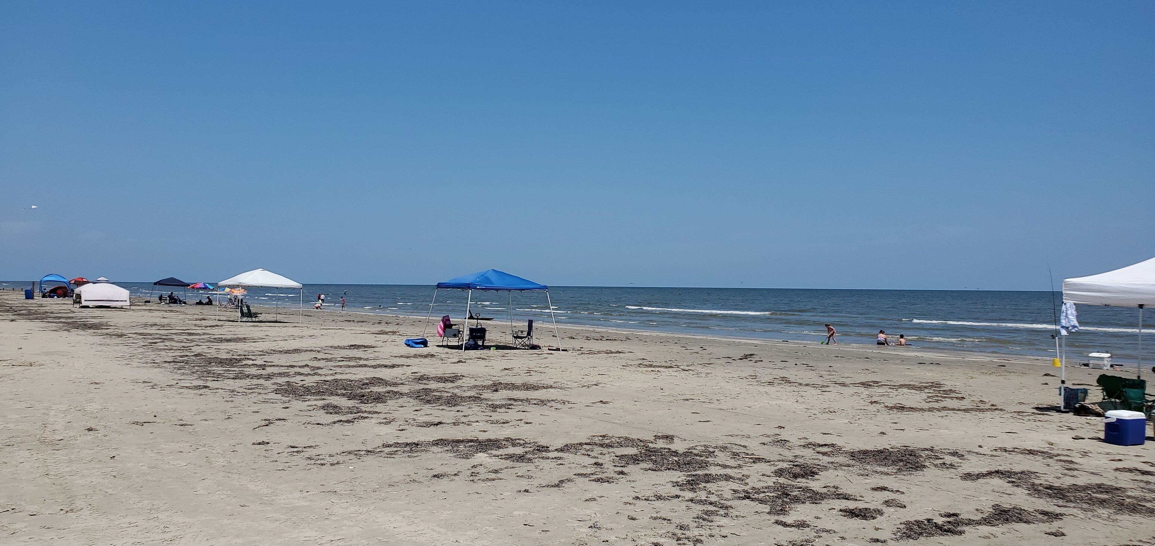A beach with tents and beach chairs, a clear sky, and the ocean.