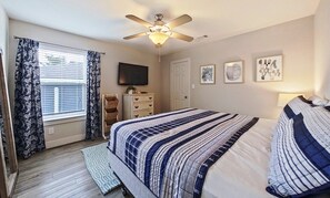 Un dormitorio con una cama, ventilador de techo, televisor y obras de arte en la pared.