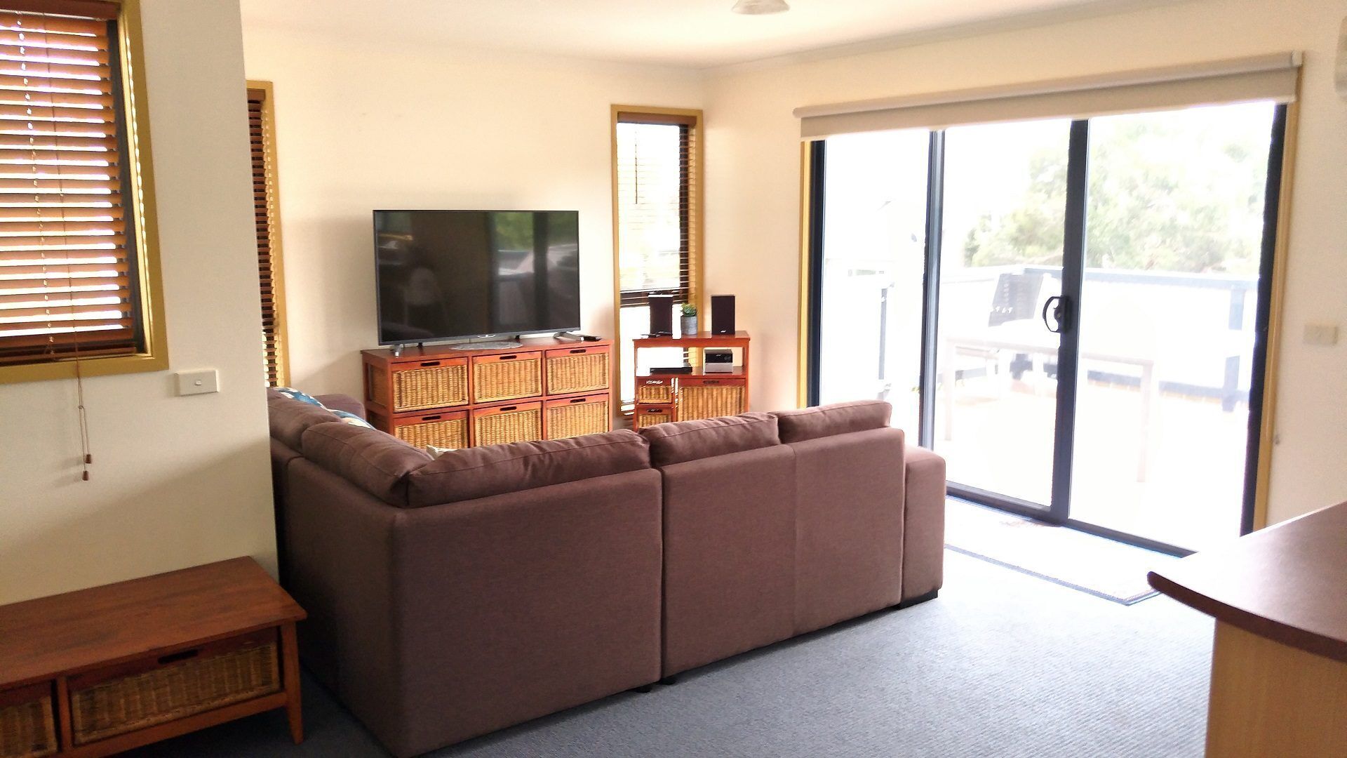 A living room with a brown sofa, a television on a wooden stand, and a sliding glass door leading outside.