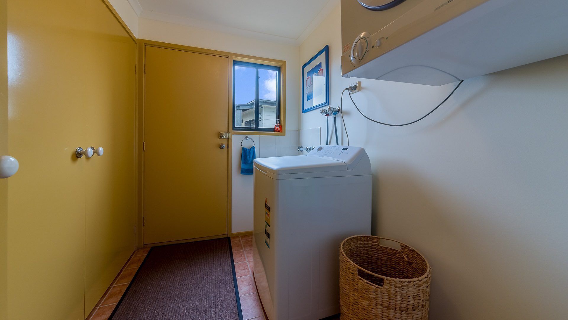 A laundry room with a washing machine, a drying rack, and a door leading to another room.