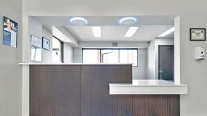 A reception area with a wooden reception desk, a white counter, and a colorful striped rug on the floor. - Studio 6 Waco, TX - Downtown - Baylor (Waco)