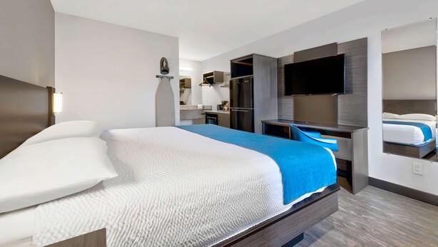 A modern hotel room with a large bed, a desk, a flat-screen TV, and a built-in wardrobe. - Studio 6 Waco, TX - Downtown - Baylor (Waco)
