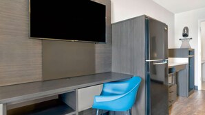 A modern kitchen with a built-in TV, a blue chair, and a refrigerator. - Studio 6 Waco, TX - Downtown - Baylor (Waco)