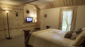 A cozy bedroom with a wooden wall, a bed with beige bedding, a desk with a computer, and a standing lamp.