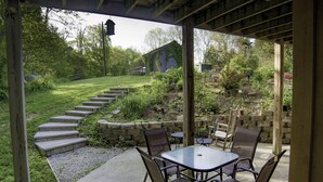 An outdoor patio with a table and chairs, surrounded by a stone wall and steps leading to a grassy area.