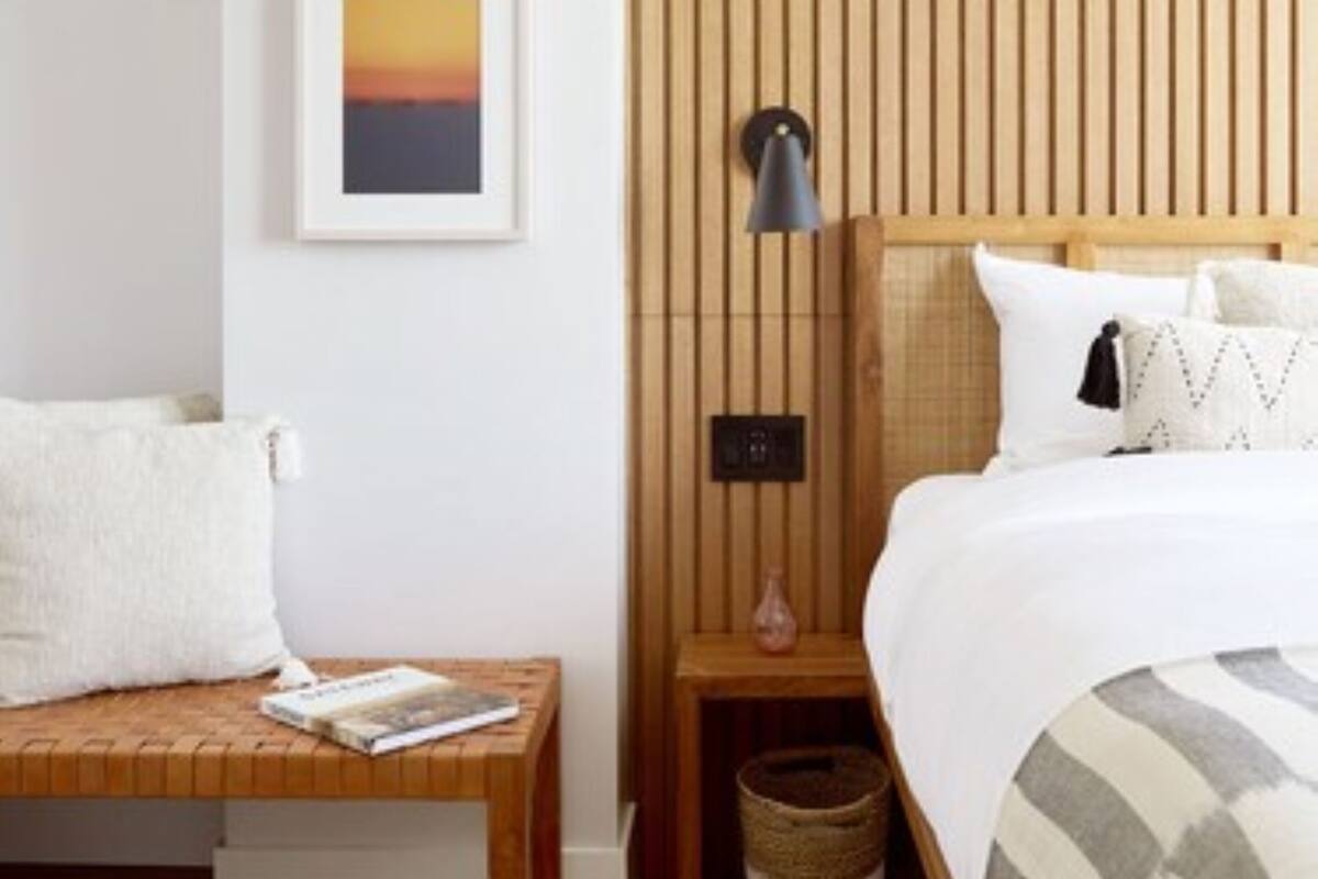 A bedroom with a wooden slat headboard, a bed with white bedding, a bedside table with a lamp, and a framed picture on the wall.