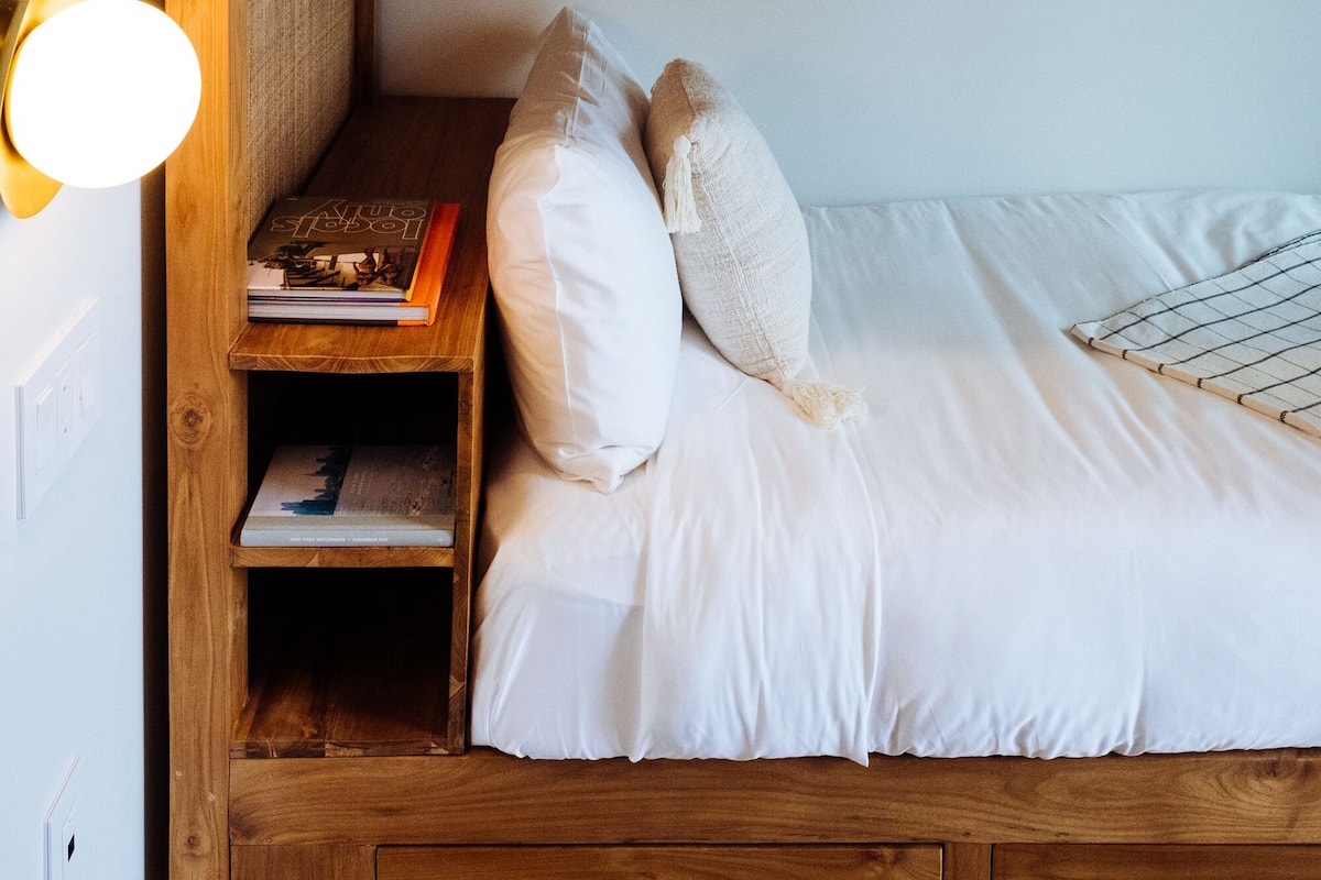 A bunk bed with a wooden headboard, a bedside table with a lamp, and a shelf with books.