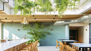 A spacious indoor area with a long wooden table and chairs, a large potted plant, and hanging greenery.
