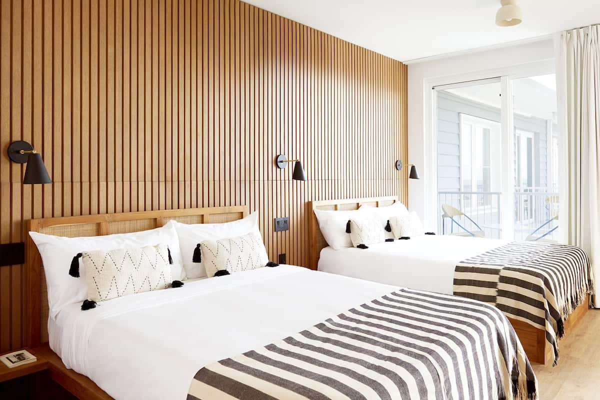 A hotel room with two beds, wooden panel walls, and a balcony with a railing.