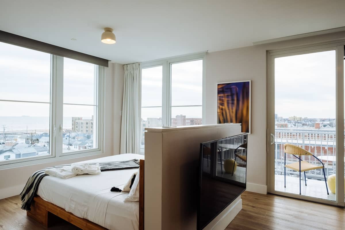 A modern hotel room with a large bed, a TV, and a balcony with a chair.