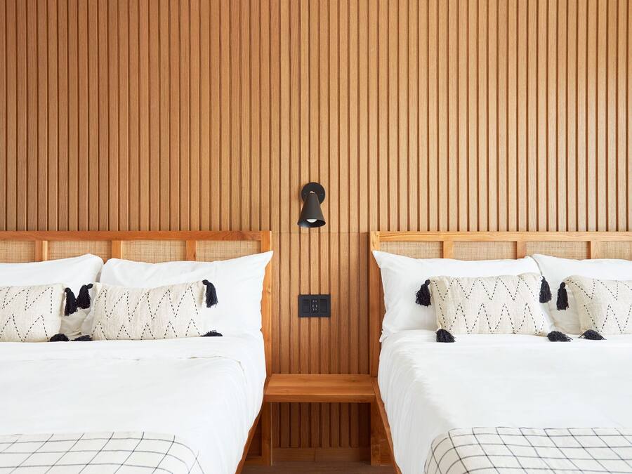 Une chambre d’hôtel avec deux lits, des murs lambrés, un petit banc en bois et un luminaire fixé au mur.
