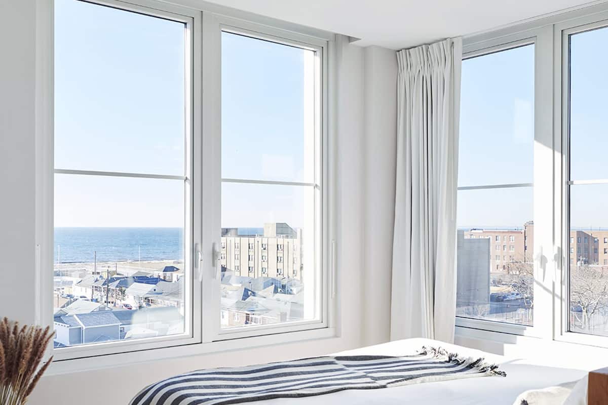 A bedroom with a large bed, a view of the city, and a window with curtains.