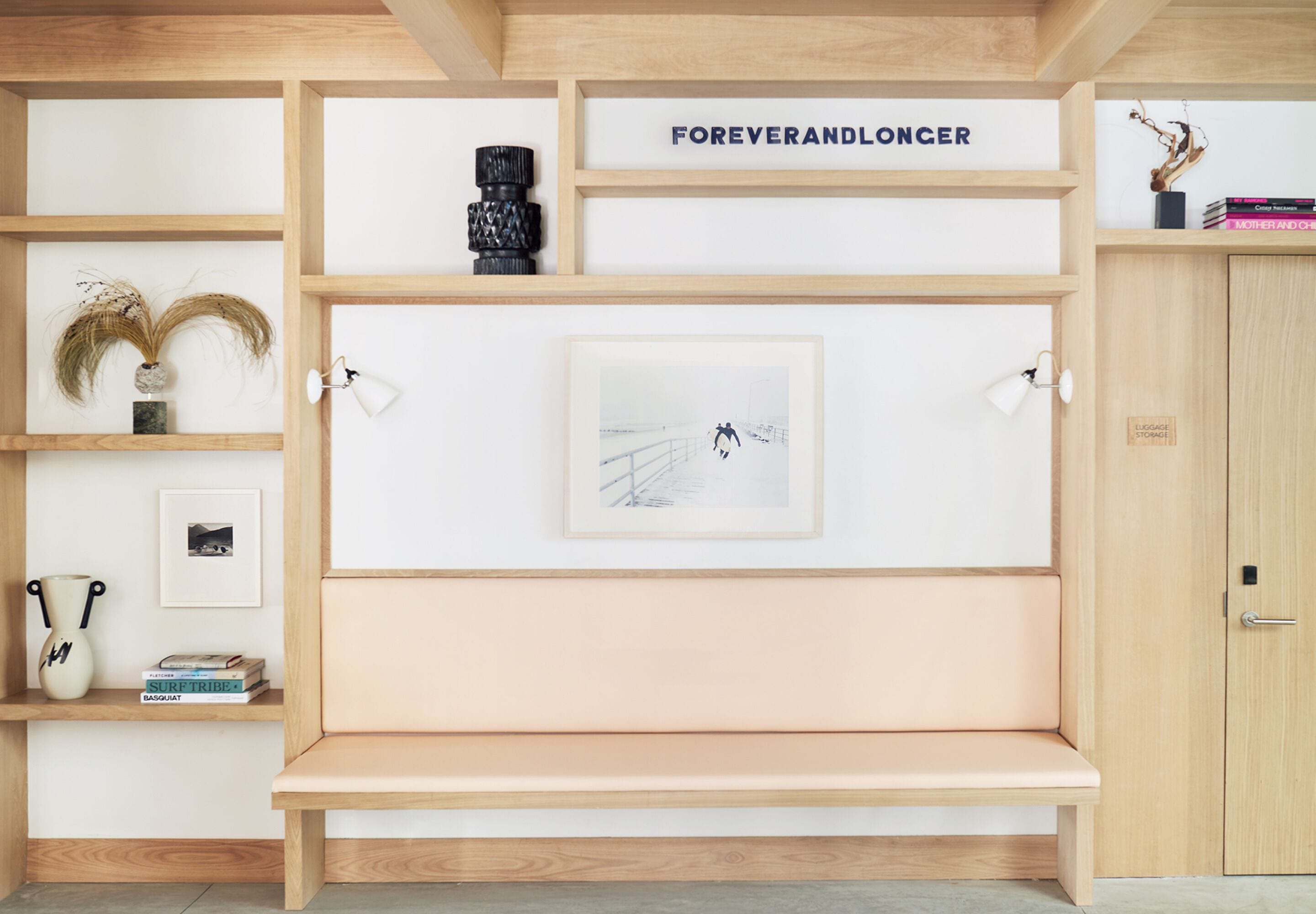 Habitación minimalista con un banco de madera, un cuadro enmarcado y una estantería con libros y adornos.