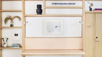 Habitación minimalista con un banco de madera, un cuadro enmarcado y una estantería con libros y adornos.