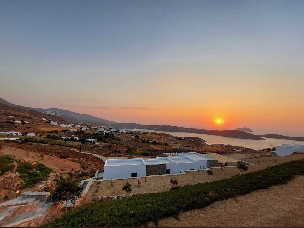 A coastal village with white buildings and a clear view of the sunset over the sea.
