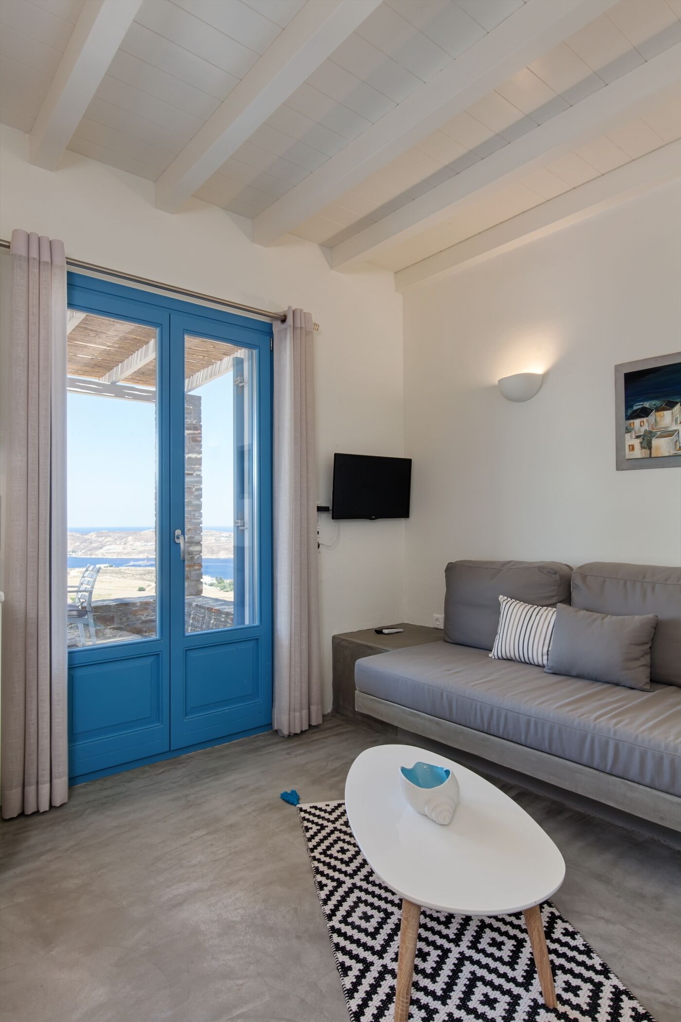 A modern living room with a blue door, a grey sofa, a white coffee table, and a TV mounted on the wall.