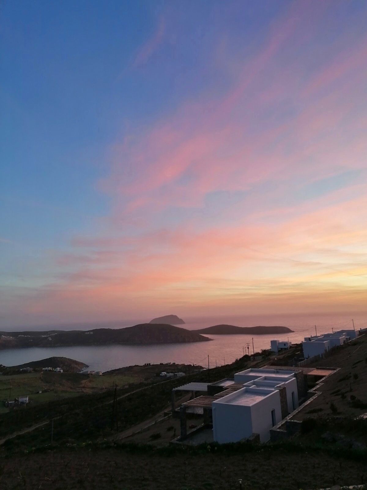 Paisagem costeira com céu claro, corpo d'água e vários edifícios com telhados planos.
