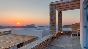 Eine Dachterrasse mit Steinmauern, einer Pergola und Blick auf den Sonnenuntergang über dem Meer.
