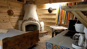 A rustic wooden room with a stone fireplace, a bed with patterned bedding, a small table with a cloth, and a coffee maker. - Little Cottage in Flagstaff (Flagstaff)