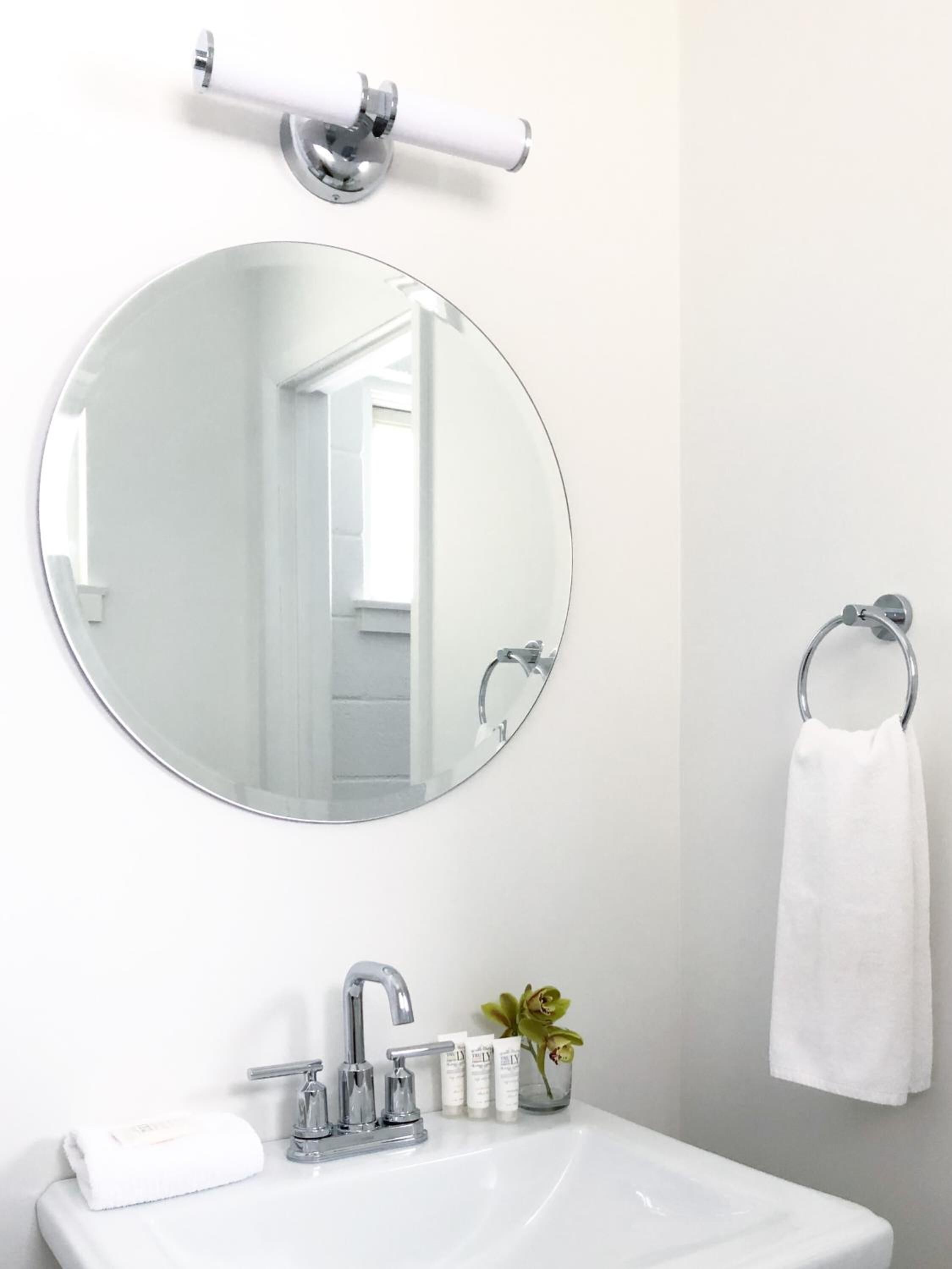 A bathroom with a round mirror, a towel ring, a sink, and toiletries.