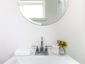 A bathroom with a round mirror, a chrome faucet, a white sink, a towel, and a small vase with flowers. - The Nomad Motel - International Falls, MN - Near Canadian Border (International Falls)