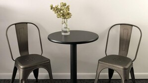 A room with a round table, two chairs, a vase with flowers, and a framed abstract painting on the wall.