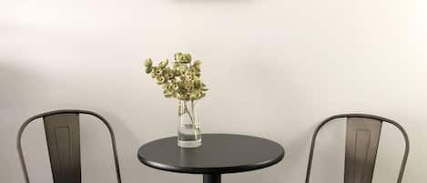 Een kamer met een ronde tafel, twee stoelen, een vaas met bloemen en een lijst met een abstract schilderij aan de muur.