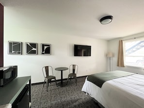A hotel room with a bed, a TV, a desk with a chair, and a small table with two chairs. - The Nomad Motel - International Falls, MN - Near Canadian Border (International Falls)