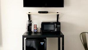 A compact kitchenette with a TV, microwave, coffee maker, and mini-fridge on a black cart.